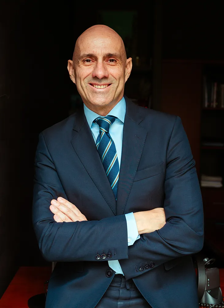 Hombre de negocios sonriente con traje y corbata, de brazos cruzados, en una oficina.