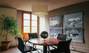 Sala de reuniones acogedora con mesa redonda, sillas modernas, plantas y arte en la pared.