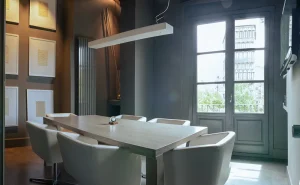 Sala de reuniones moderna con mesa de madera y sillas blancas, decorada con cuadros y una gran ventana.